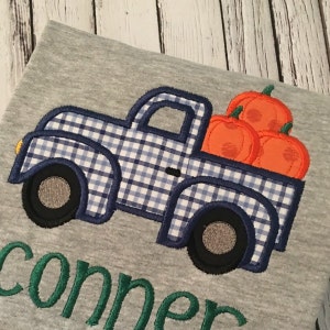May include: A gray t-shirt with a blue and white checkered truck carrying three orange pumpkins. The name "conner" is embroidered in green below the truck.