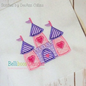 May include: Purple and pink embroidered castle design with pink hearts. The design is stitched on a white fabric. The text "Stitched by DeeAnn Collins" and "Belliboos Designs" is visible.