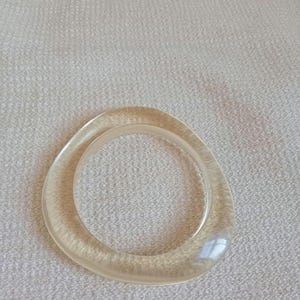 May include: A clear, oval-shaped bracelet with a smooth, polished surface. The bracelet is made of a translucent material, allowing light to pass through. The design is simple and elegant, suitable for everyday wear.