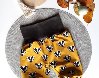 Könnte beinhalten: Gelbe Babyhose mit Dachs-Muster und grauem Bund und Bündchen. Die Hose liegt auf einer grauen, strukturierten Oberfläche.