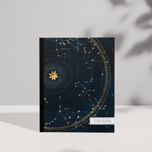 May include: A dark blue notebook featuring a gold celestial star map design with constellations and zodiac signs. A white rectangular label at the bottom right reads DOTTED BULLET JOURNAL 110 PAGES | CREAM PAPER in black text.