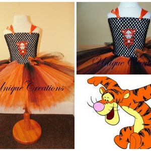 May include: A black and orange tulle tutu with a black bodice featuring a Tigger applique. The bodice has a polka dot pattern. The tutu has three layers of tulle in orange, black, and cream.