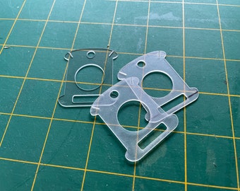 May include: Two clear plastic templates for crafting, each with a circular hole and a rectangular slot. The templates are on a green cutting mat.