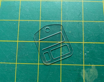 May include: A clear plastic tag with three rectangular cutouts for text or images. The tag has a hole at the top for attaching a string or ribbon.