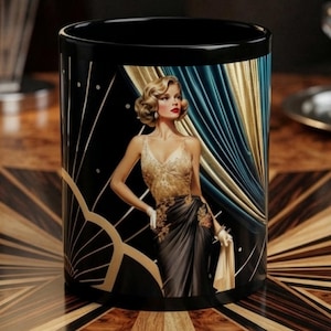 May include: A black ceramic mug featuring a graphic illustration of a person with blonde hair wearing a gold and black gown. The design includes gold fan-shaped accents, blue and gold draped curtains, and a dark background with small white dots.
