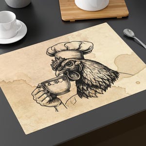May include: A sepia-toned placemat featuring a rooster in a chef's hat, drinking from a teacup. The design has coffee stain details. A white teacup and saucer are on the left. A teapot and spoon are also visible.