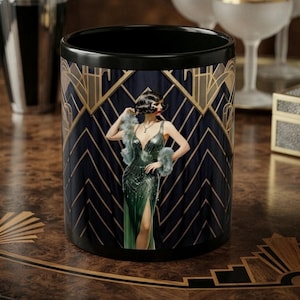 May include: A black ceramic mug featuring a graphic illustration of a person in a green sequined gown with a high slit and a grey fur stole. The background displays a dark blue and gold geometric art deco pattern with sharp angular lines.