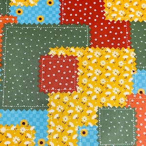 May include: A patchwork fabric featuring rectangular and square segments with pinked edges. The pattern includes yellow sunflowers on blue, white daisies on yellow, white hearts on green, and white floral prints on red and orange backgrounds.