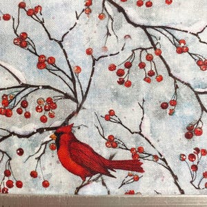 May include: Fabric with a winter scene featuring red cardinals perched on branches with red berries against a light blue background. The branches are dark brown, and the berries are clustered. The fabric has a textured appearance.