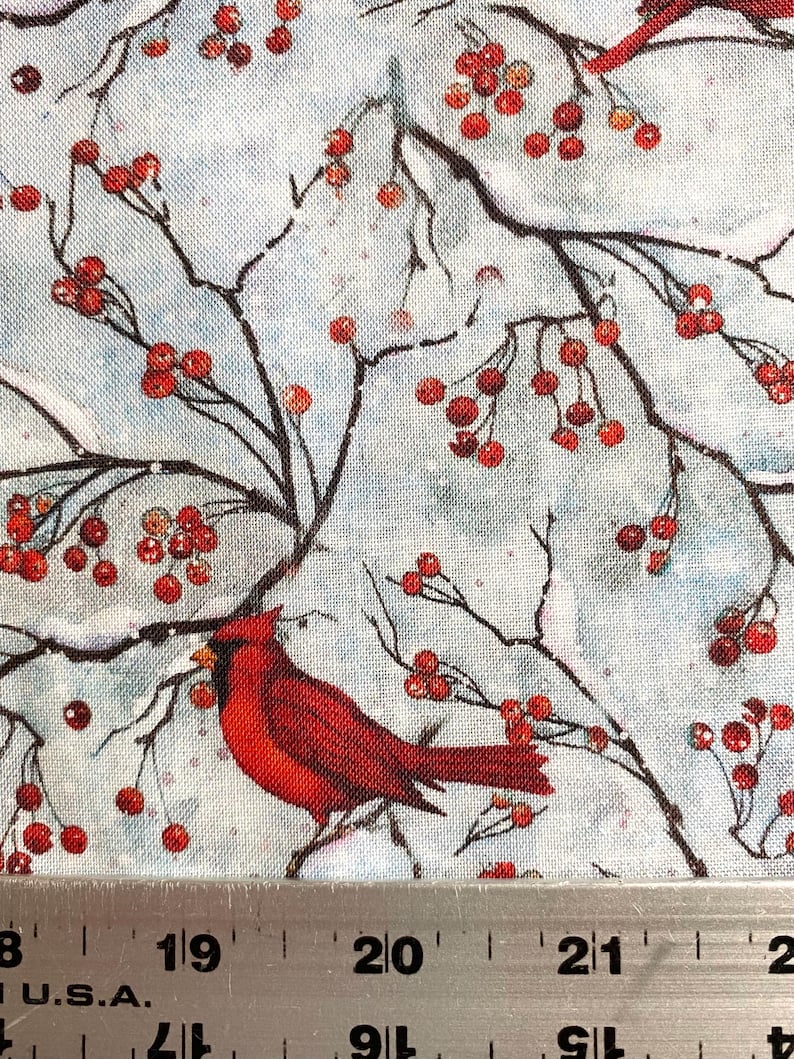 May include: Fabric with a winter scene featuring red cardinals perched on branches with red berries against a light blue background. The branches are dark brown, and the berries are clustered. The fabric has a textured appearance.