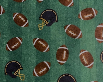 May include: A green fabric featuring a repeating pattern of brown American footballs and black helmets with yellow face masks. The footballs have white laces and stripes. The background has vertical green stripes.