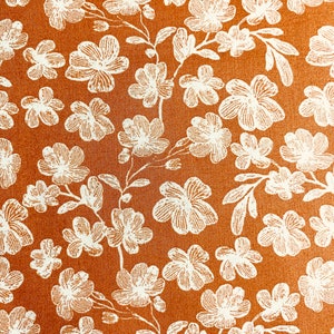 May include: A brown fabric with a white floral pattern. The flowers are small and delicate, and they are arranged in a repeating pattern.
