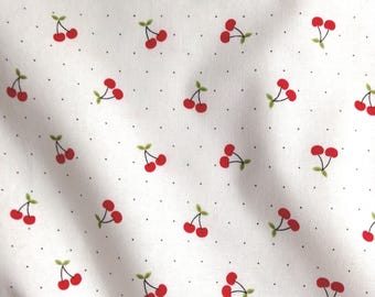May include: A white fabric featuring a repeating pattern of small red cherries with green stems and leaves, interspersed with tiny black polka dots. The material has a soft, folded texture that creates subtle shadows across the surface.