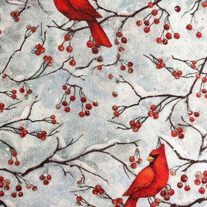 May include: A fabric design featuring two vibrant red cardinal birds perched on snow-covered branches with clusters of red berries. The background is a soft, light blue with a subtle snowy texture, creating a wintery scene.