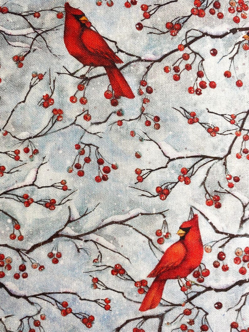 May include: A fabric design featuring two vibrant red cardinal birds perched on snow-covered branches with clusters of red berries. The background is a soft, light blue with a subtle snowy texture, creating a wintery scene.