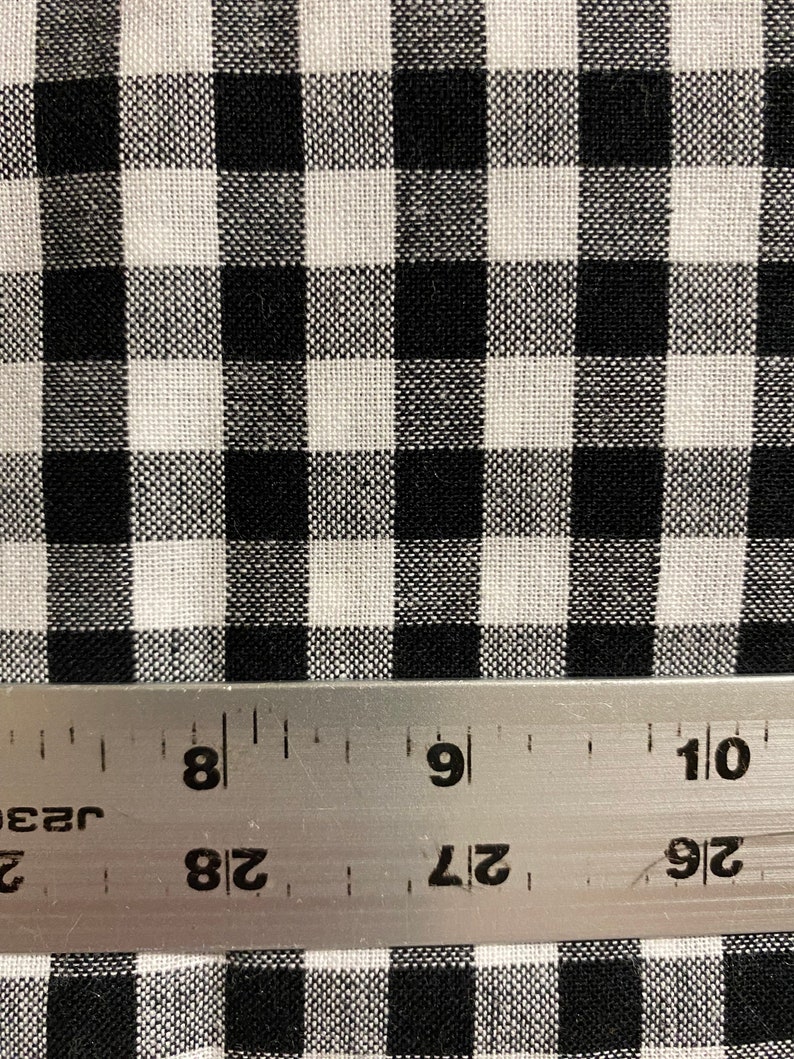 May include: Black and white gingham fabric with a ruler showing 8 inches. The fabric has a small check pattern.