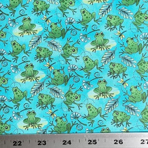 May include: A turquoise fabric with a repeating pattern of green frogs, leaves, and flowers. The fabric is measured with a ruler in inches.