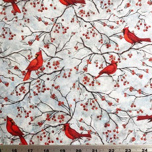May include: Fabric with a repeating pattern of red cardinals perched on branches with red berries against a light blue background. The branches are dark brown, and the berries are small and round. The fabric is measured in inches.