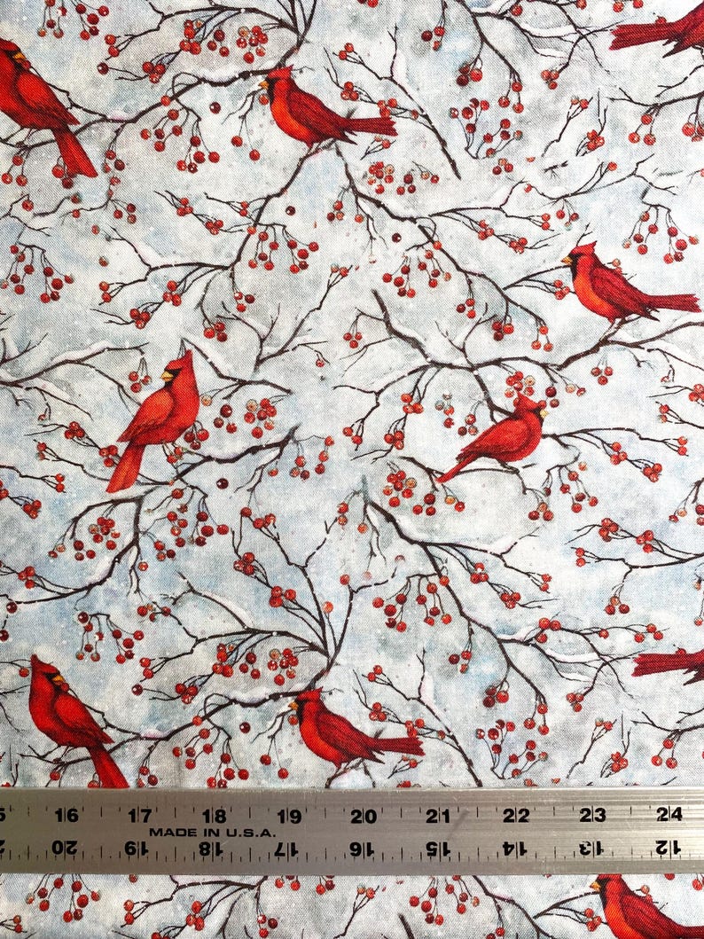 May include: Fabric with a repeating pattern of red cardinals perched on branches with red berries against a light blue background. The branches are dark brown, and the berries are small and round. The fabric is measured in inches.