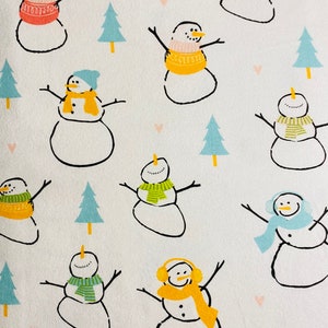May include: White background with a repeating pattern of snowmen and small blue Christmas trees. The snowmen have black outlines, stick arms, and are wearing colorful scarves, hats, and earmuffs in shades of pink, yellow, and green. Some have carrot noses.