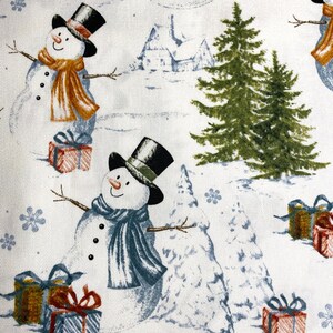 Puede incluir: Tela blanca con un patr&oacute;n repetido de mu&ntilde;ecos de nieve, pinos, copos de nieve y regalos envueltos. Los mu&ntilde;ecos de nieve llevan sombreros de copa negros y bufandas en tonos naranja y azul. Los regalos est&aacute;n envueltos en rojo, azul y dorado.