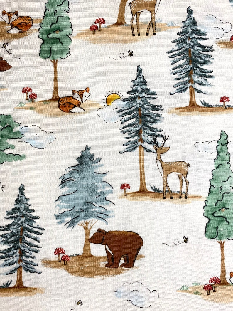 May include: A white fabric with a repeating pattern of brown bears, deer, foxes, and pine trees. The background is a light cream color with brown and green accents.