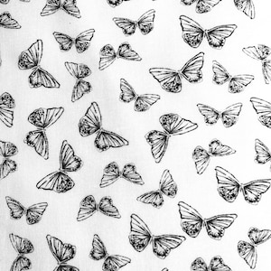 May include: White fabric with a repeating pattern of black butterflies. The butterflies are all different sizes and shapes, and they are arranged in a random pattern.