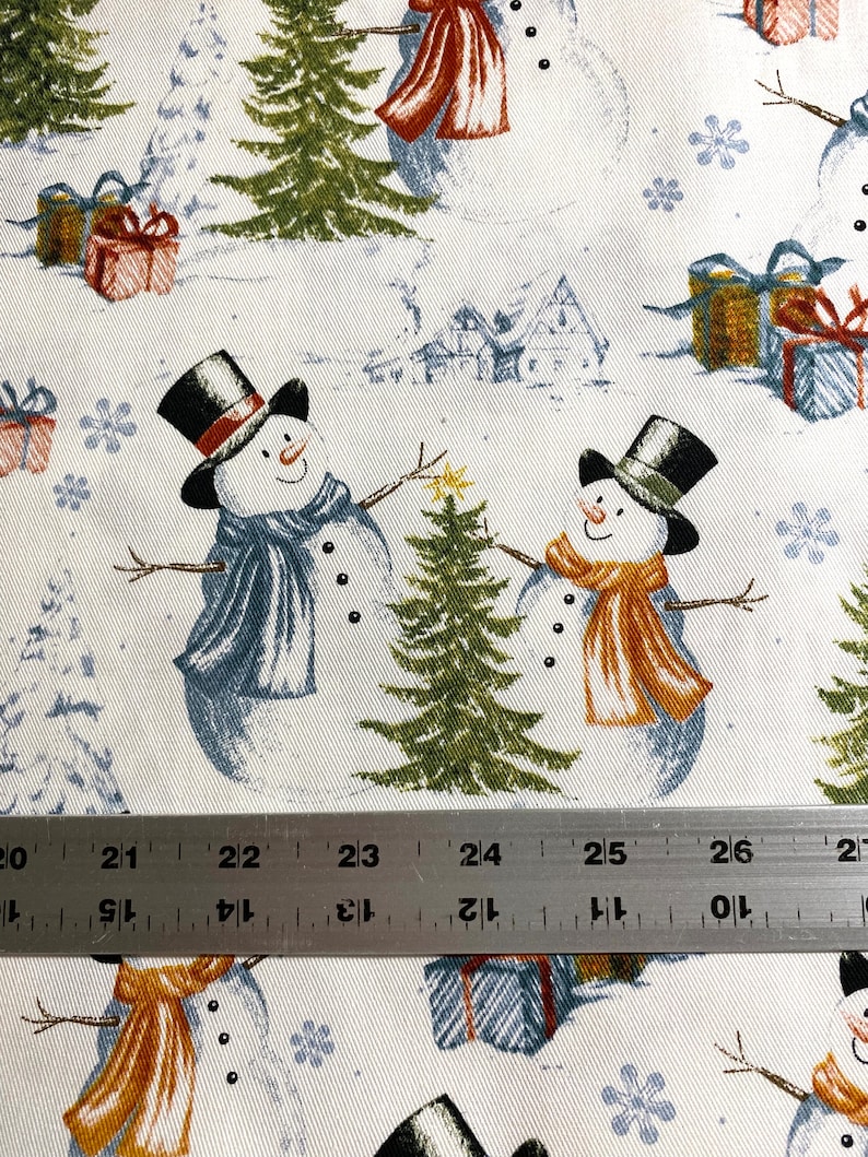 Puede incluir: Tela blanca con un patr&oacute;n repetido de mu&ntilde;ecos de nieve, &aacute;rboles de Navidad, copos de nieve y regalos envueltos. Los mu&ntilde;ecos de nieve llevan sombreros de copa y bufandas. Los regalos tienen envoltorios azules, rojos y dorados. Los &aacute;rboles son verdes.
