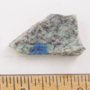 Könnte beinhalten: Ein kleiner, unregelmäßig geformter Stein mit einer Mischung aus Farben. Der Stein hat eine gesprenkelte grau-weiße Basis mit blauen und grünen Flecken. Der Stein ist etwa 5 cm lang.