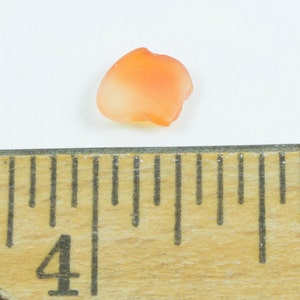 May include: A small, orange, petal-shaped object with a gradient from light to dark orange. The object is next to a wooden ruler, with the 4-inch mark visible. The object appears to be made of a translucent material.
