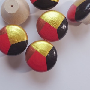 Könnte beinhalten: Sechs Holzgriffe mit geometrischem Design. Die Griffe sind in Rot, Schwarz und Gold lackiert.
