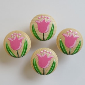 Könnte beinhalten: Vier Holzknöpfe mit darauf gemalten pinkfarbenen Tulpenblumenmotiven. Die Knöpfe sind rund und haben eine helle Holzoptik.