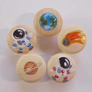 Könnte beinhalten: Fünf Holzgriffe mit bemalten Designs zum Thema Weltraum. Die Griffe zeigen einen Astronauten, einen Kometen, einen Planeten und eine Darstellung der Erde.