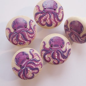 Könnte beinhalten: Fünf Holzgriffe mit lila Tintenfisch-Illustrationen. Der Tintenfisch hat einen runden Körper und acht Tentakel. Die Griffe sind rund und haben eine glatte Oberfläche.