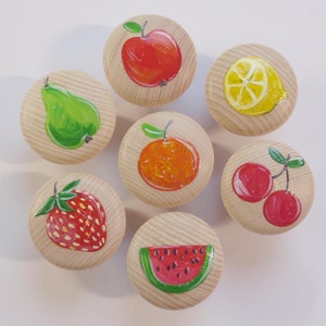Könnte beinhalten: Sieben Holzgriffe, die mit verschiedenen Früchten bemalt sind: ein roter Apfel, eine grüne Birne, eine orangefarbene Orange, zwei rote Kirschen, eine gelbe Zitrone und eine rote Wassermelonen-Scheibe.