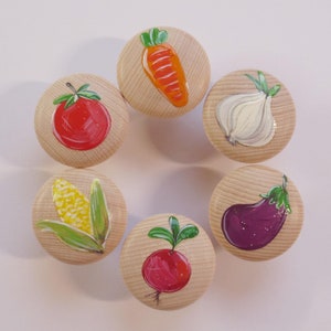 Könnte beinhalten: Sechs Holzgriffe, die mit verschiedenen Gemüsesorten bemalt sind. Die Griffe sind rund und haben eine hellbraune Farbe. Das Gemüse sind eine rote Tomate, ein gelber Maiskolben, eine lila Aubergine, ein roter Radieschen, eine Karotte und eine weiße Knoblauchzehe.