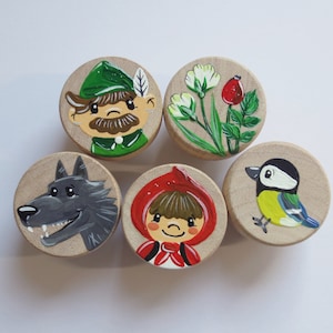 Könnte beinhalten: Fünf Holzrundungen mit gemalten Bildern aus dem Märchen Rotkäppchen. Die Kreise zeigen einen Wolf, ein kleines Mädchen in einer roten Kapuze, einen Vogel, einen Jäger und einen Rosenstrauch.