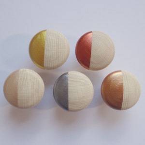 Könnte beinhalten: Sechs runde Holzgriffe mit einem Halbkreis aus Metallic-Farbe auf einer Seite. Die Griffe sind in Gold, Kupfer, Silber und Rot lackiert.