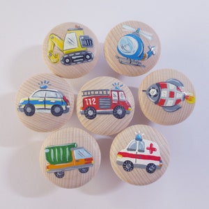 Könnte beinhalten: Satz von sieben Holzgriffen mit bemalten Bildern von Fahrzeugen, darunter ein Polizeiauto, ein Feuerwehrauto, ein Krankenwagen, ein Bagger, ein Hubschrauber, eine Rakete und ein Betonmischer. Die Griffe sind in leuchtenden Farben bemalt und haben ein verspieltes Design.