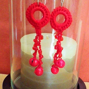 May include: A pair of red crocheted earrings with dangling beads. The earrings are hanging from a glass jar with a candle inside.