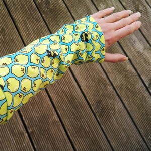 Pu&ograve; includere: Primo piano di una manica con un motivo vivace. Il tessuto presenta un motivo ripetuto di limoni gialli su sfondo azzurro. Il polsino &egrave; abbottonato. Lo sfondo &egrave; una superficie di legno.