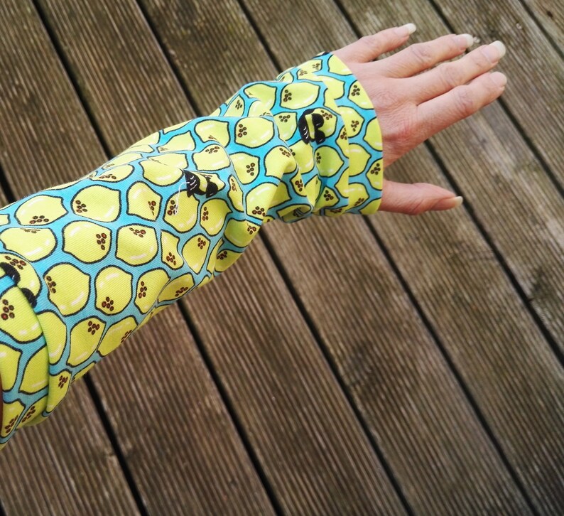 Pu&ograve; includere: Primo piano di una manica con un motivo vivace. Il tessuto presenta un motivo ripetuto di limoni gialli su sfondo azzurro. Il polsino &egrave; abbottonato. Lo sfondo &egrave; una superficie di legno.