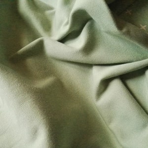 Puede incluir: Primer plano de una tela suave de color verde con textura arrugada. La tela es lisa y parece estar hecha de algodón.