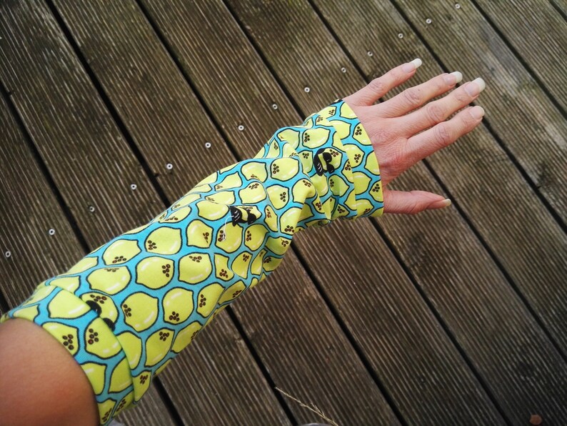 Pu&ograve; includere: Un manicotto a maniche lunghe con un motivo a limone. Il tessuto &egrave; giallo con un motivo a nido d'ape azzurro e illustrazioni di limoni neri. Il manicotto &egrave; indossato sul braccio.