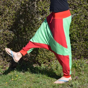 May include: A person wearing green and red pants with a unique design. The pants are loose fitting and have a wide leg. The person is wearing flip flops.