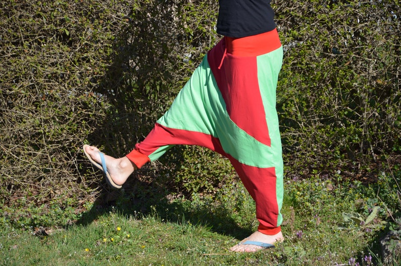May include: A person wearing green and red pants with a unique design. The pants are loose fitting and have a wide leg. The person is wearing flip flops.