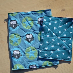 May include: Two blue fabric squares with different patterns. One square has a pattern of owls and stars, the other has a pattern of white stars on a blue background.