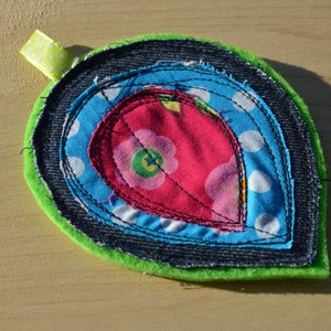 May include: A green, blue, white, and pink fabric heart with a decorative stitch pattern. The heart is made of multiple layers of fabric and has a loop for hanging.