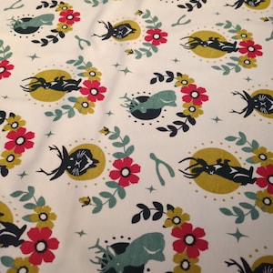 Könnte beinhalten: Weißer Stoff mit einem sich wiederholenden Muster aus schwarzen Hirschen, teal Walen und gelben Monden, umgeben von roten und gelben Blumen und grünen Blättern. Das Design enthält auch Wunschknochen und Sterne.