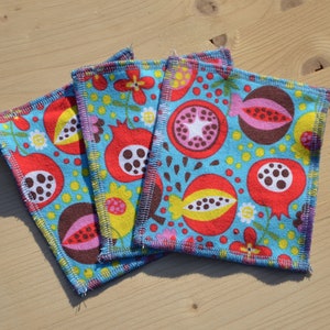 May include: Four blue fabric squares with a colorful pomegranate pattern. The squares have a zig-zag stitch around the edges.